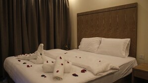Una cama bien hecha con ropa de cama y toallas blancas, un cabecero de madera y una mesita de noche con una lámpara.