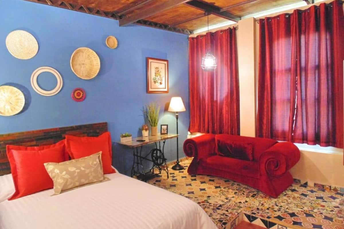 A bedroom with a bed, red sofa, and a table with a lamp.