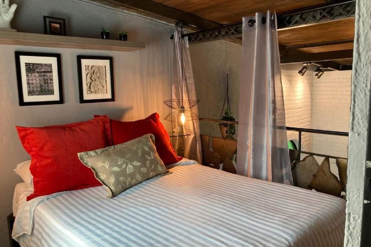 A bed with striped bedding, red and beige pillows, and a wall-mounted light fixture.