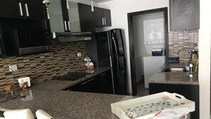 A modern kitchen with black cabinets, a granite countertop, a built-in oven, and a refrigerator. - Golden Mar Hostal (Manta)