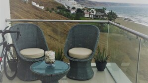 A balcony with wicker chairs and a small table, overlooking a beach and white buildings. - Golden Mar Hostal (Manta)
