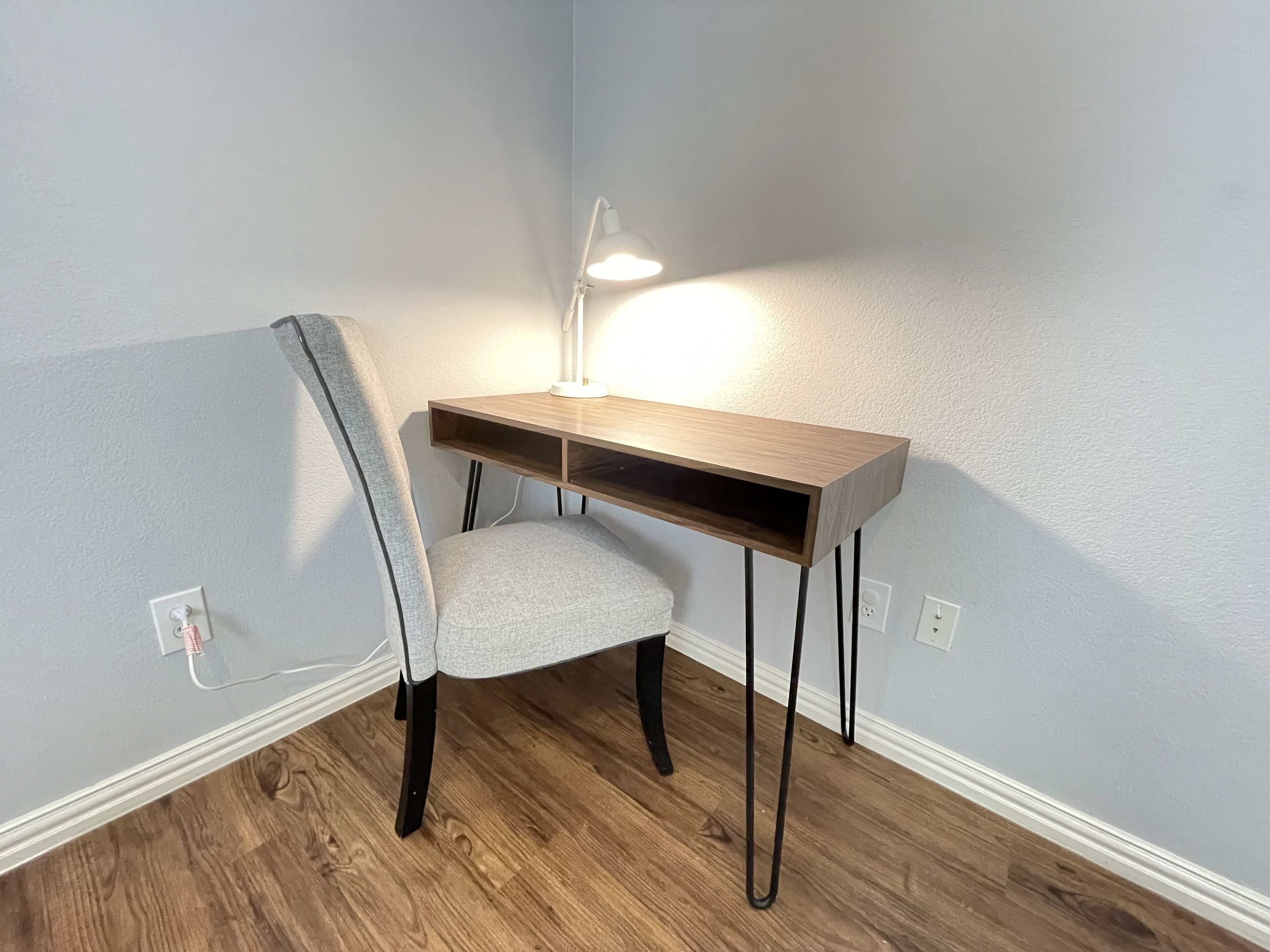 Et hjørnebord med stol, en skrivebordslampe og en stikkontakt på væggen.