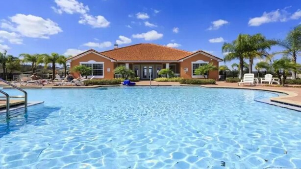 A swimming pool with a clear blue water surface, surrounded by lounge chairs and palm trees. - Crystal Cove Resort (Kissimmee)