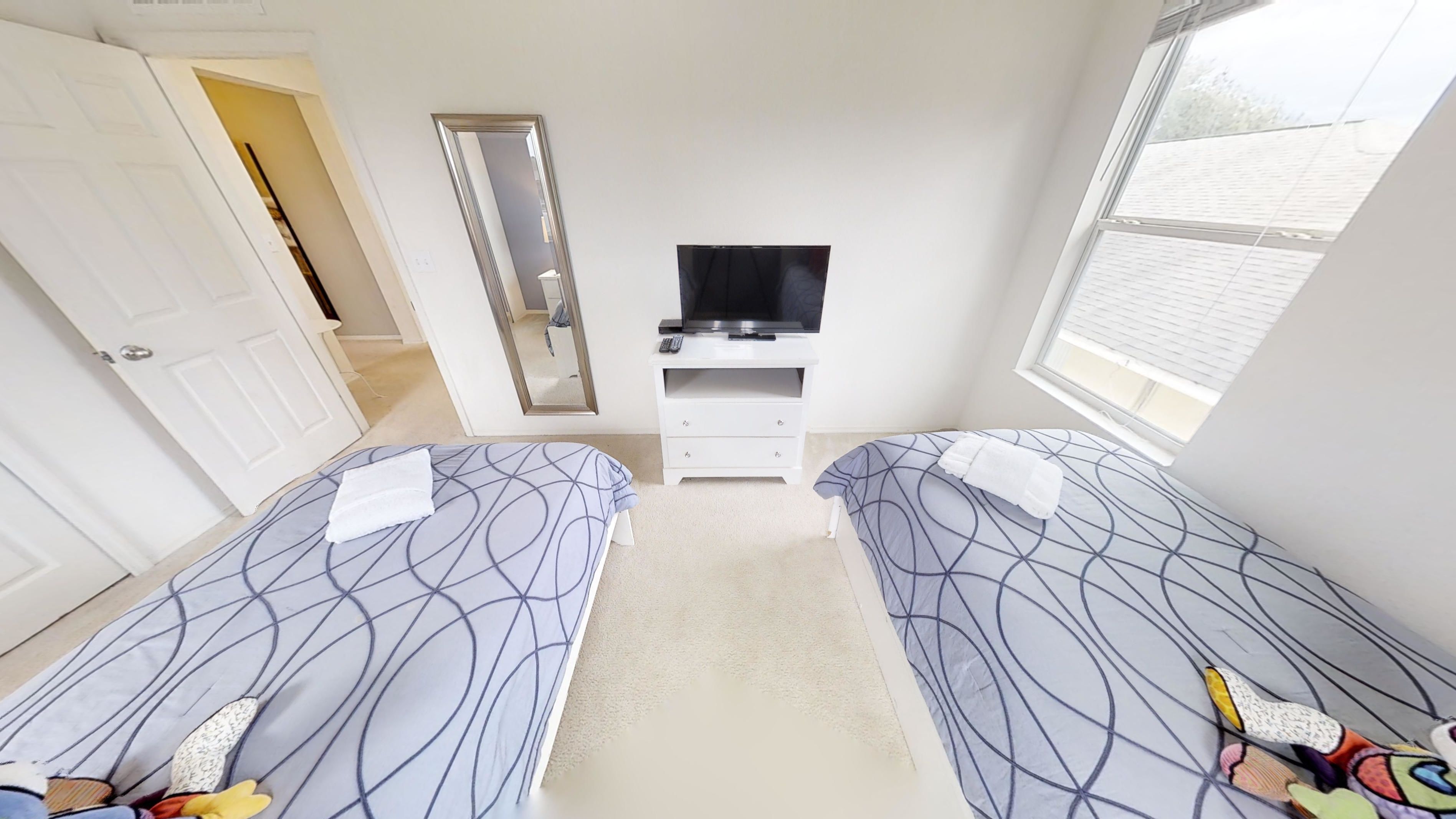 Ein Schlafzimmer mit zwei Betten, einem Fernseher, einem Schminktisch und einem Fenster.
