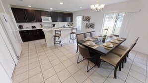 A modern kitchen with dark cabinets, a white microwave, and a central island with bar stools. - Crystal Cove Resort (Kissimmee)