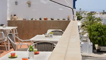 A rooftop terrace with outdoor seating, a tiled wall, and potted plants.