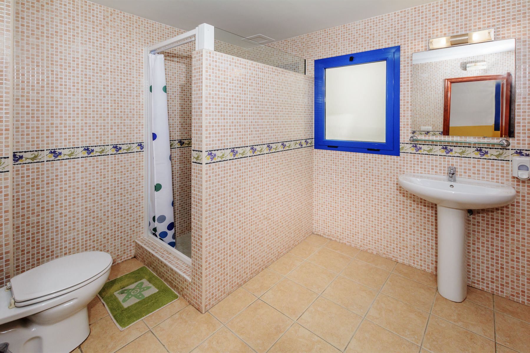 A bathroom with a toilet, shower, sink, and mirror.