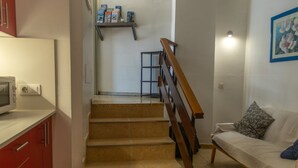 A staircase leading to a landing with a microwave on a counter, a sofa with a cushion, and a shelf with books and boxes. - Pensión MAGEC (Tías)