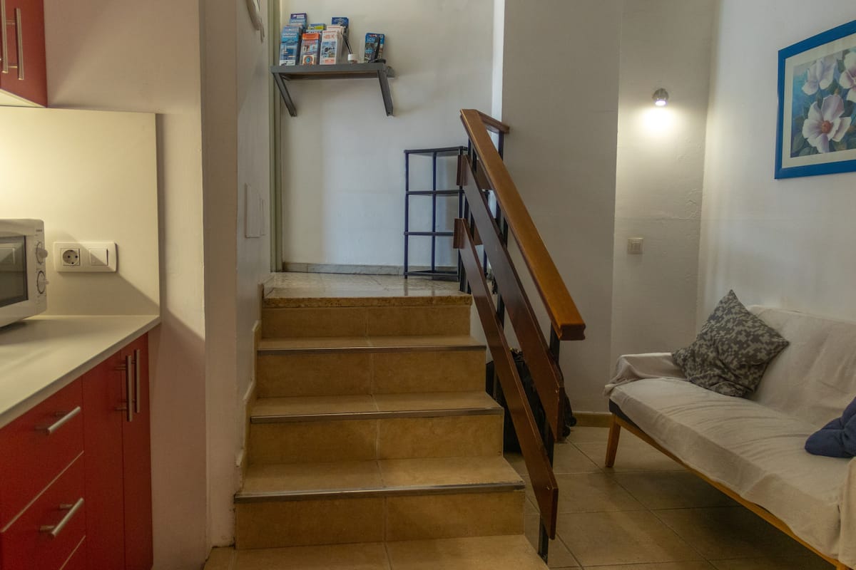 A staircase leading to a landing with a microwave on a counter, a sofa with a cushion, and a shelf with books and boxes.
