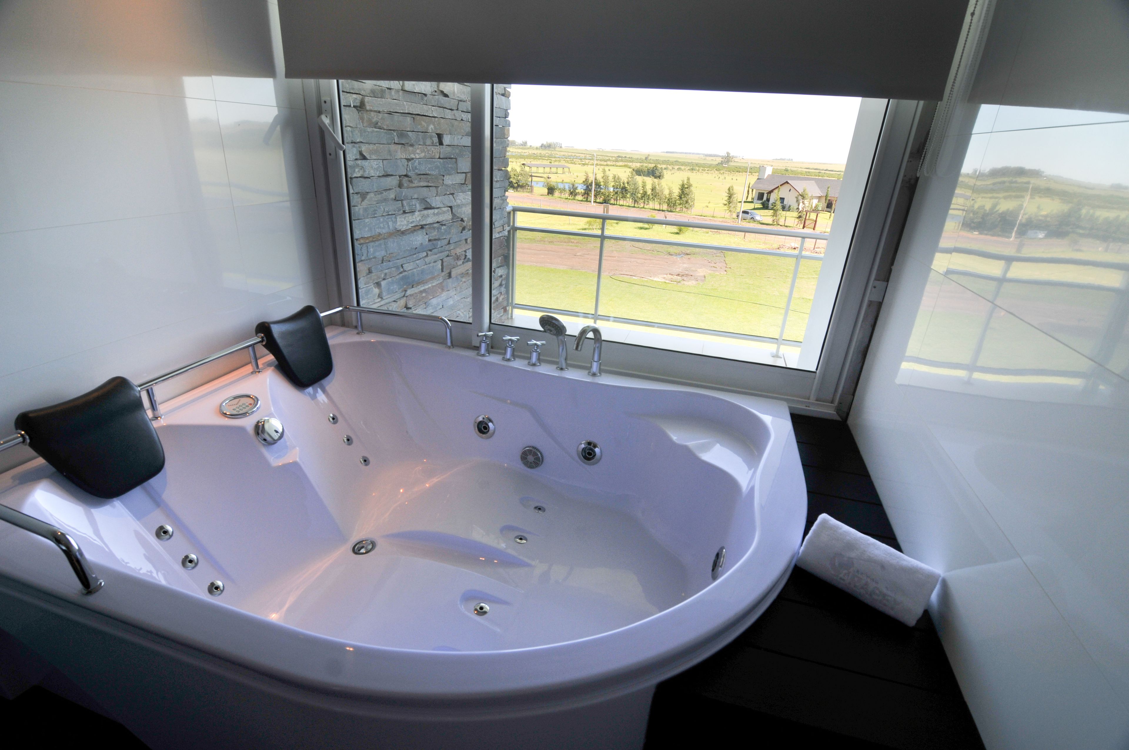 A modern bathroom with a large bathtub, a stone accent wall, and a view of a green landscape through a large window.