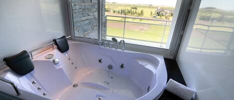 A modern bathroom with a large bathtub, a stone accent wall, and a view of a green landscape through a large window.
