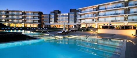 A modern hotel with a pool area, multiple balconies, and a well-lit facade.