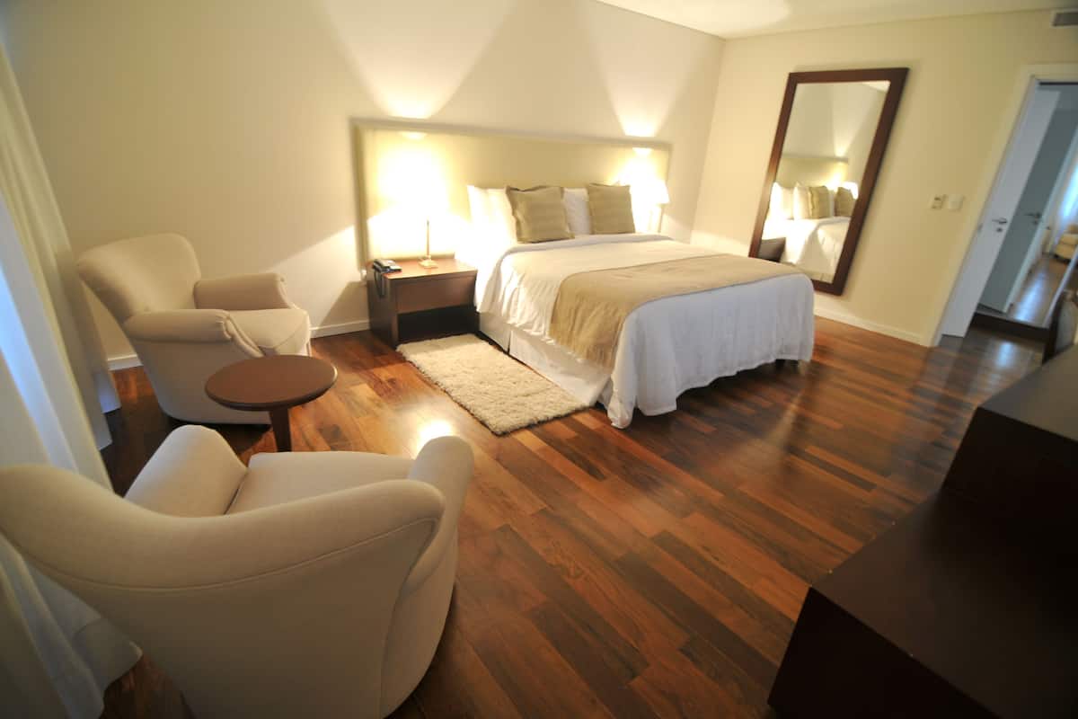 Een slaapkamer met een bed, twee nachtkastjes, een stoel, een klein tafeltje en een spiegel.