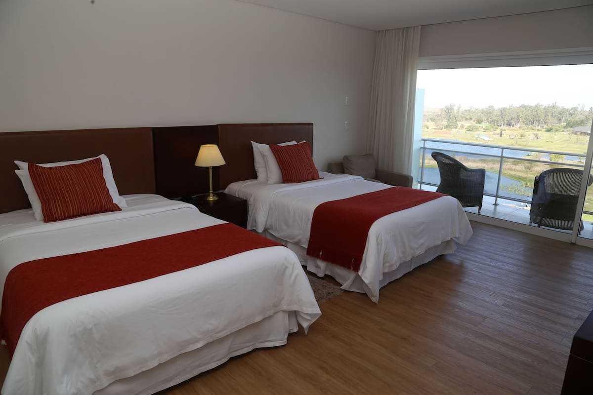 Hotelkamer met twee bedden, een nachtkastje, een lamp en uitzicht op water en groen.