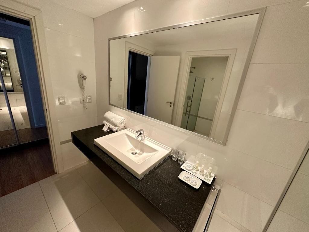 Un baño moderno con un espejo grande, un lavabo blanco y una encimera negra.