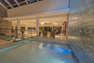 An indoor swimming pool with a glass barrier, stone walls, and a chandelier.