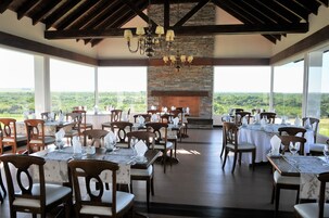 A dining area with tables set for a meal, a fireplace, and a view of the landscape.