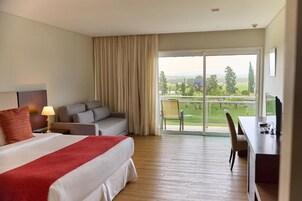 A hotel room with a bed, a desk, a sofa, and a balcony with a view of the countryside.