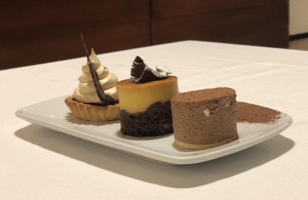 A white plate with three desserts on a table.