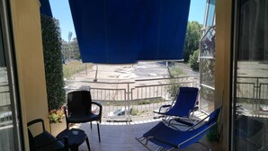 A balcony with two blue chairs and a small table, overlooking a parking area and buildings. - ViOletta (Rome)