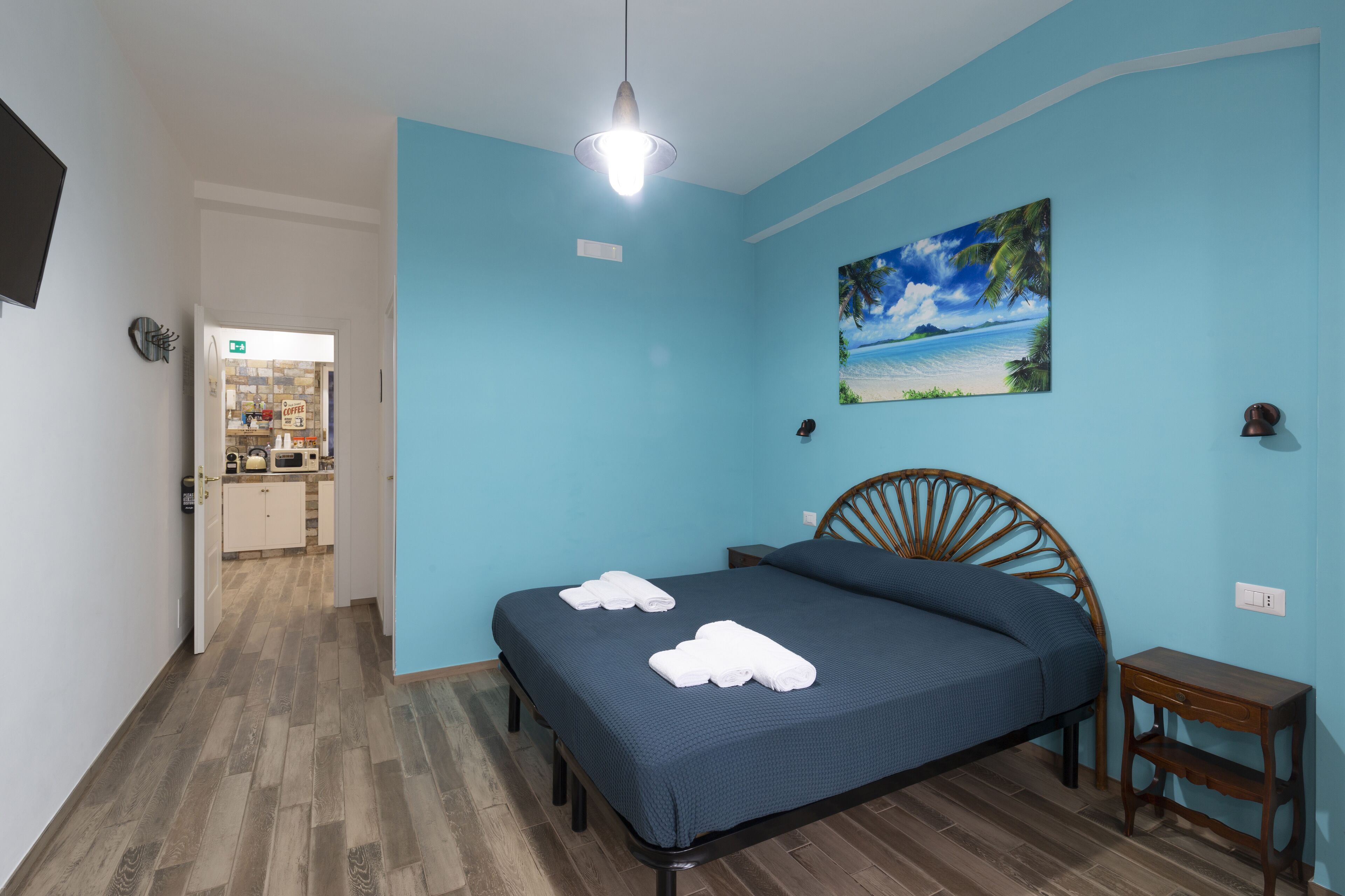 Un dormitorio con cama, cabecera de madera, mesita de noche y un cuadro de una playa.