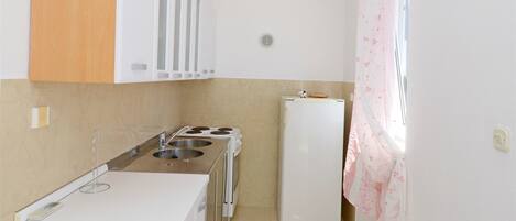 Una cocina compacta con gabinetes blancos, encimera de madera, estufa y refrigerador.