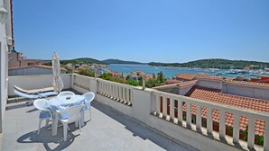 A balcony with a table and chairs, overlooking a marina with boats and a coastal town. - Apartments Branislav (Rogoznica)