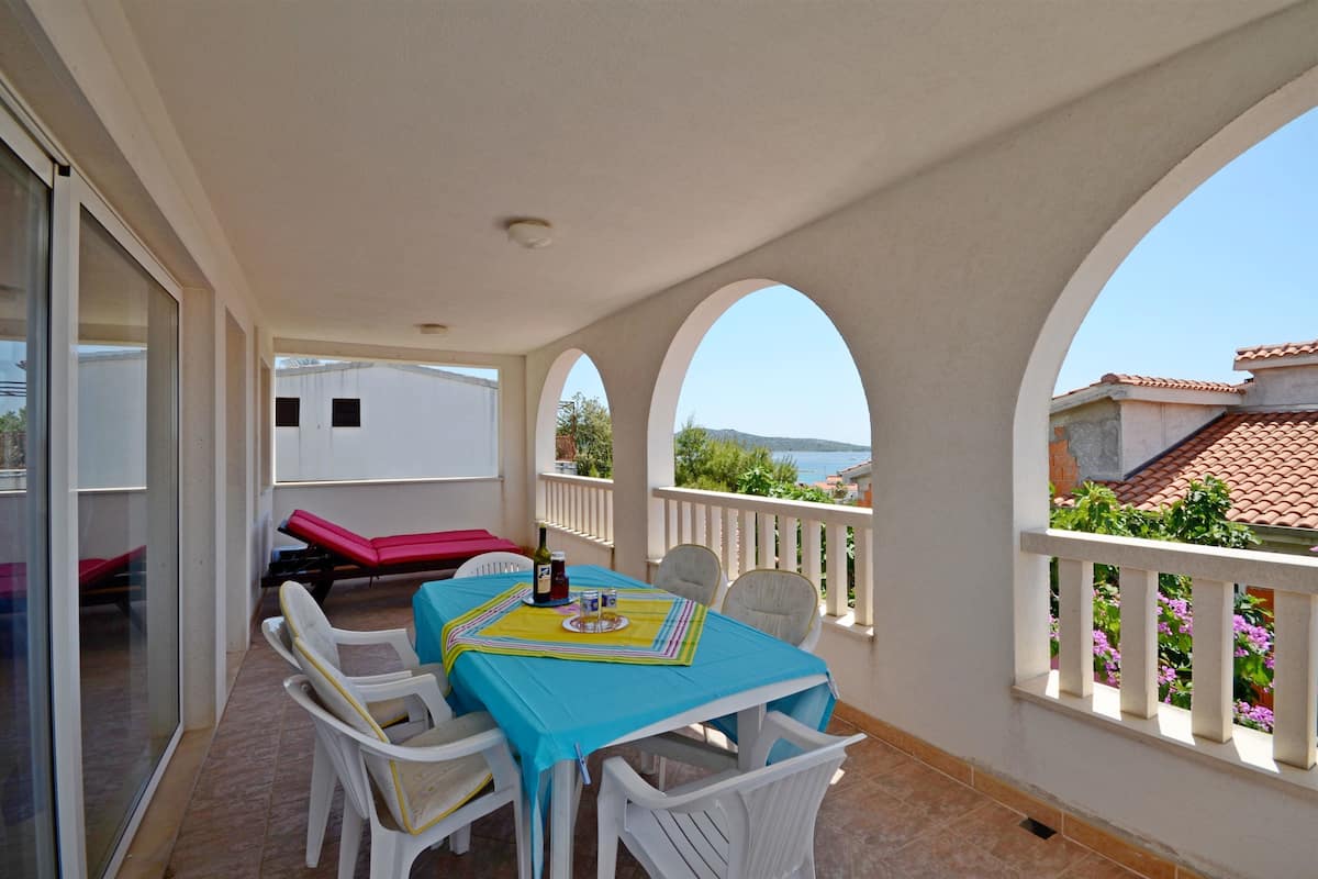 A balcony with a table and chairs, a red lounge chair, and a view of the sea.