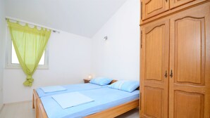 A bedroom with a single bed, a nightstand, a wardrobe, and a window with a green curtain. - Apartments Branislav (Rogoznica)