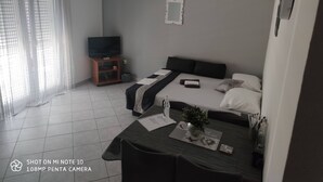 Une chambre d’hôtel moderne, équipée d’un lit, d’une télévision, d’une petite table avec une plante et d’une fenêtre avec des rideaux.