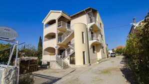Un immeuble à plusieurs étages, avec un escalier menant aux étages supérieurs, une enseigne indiquant un lieu, et une voiture garée devant.