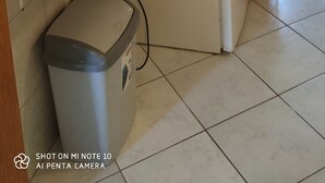Une cuisine avec des meubles de rangement en bois, un four à micro-ondes, un lave-linge et une poubelle.