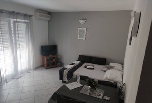 Ein modernes Hotelzimmer mit Bett, Fernseher, einem kleinen Tisch mit Pflanze und einem Fenster mit Vorhängen.