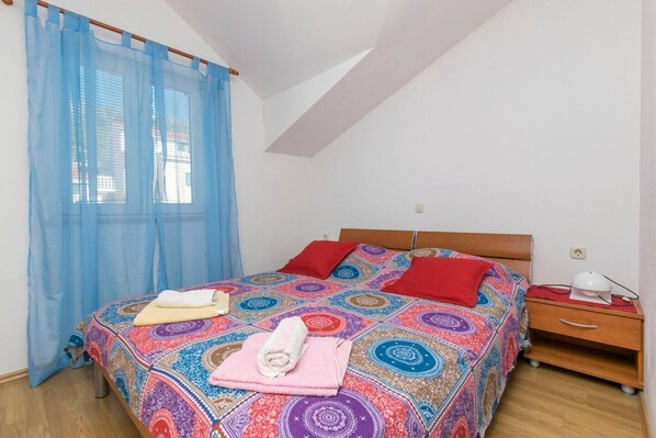 A bedroom with a bed, a nightstand, a lamp, and a window with blue curtains. - Apartments Jerka (Bol)