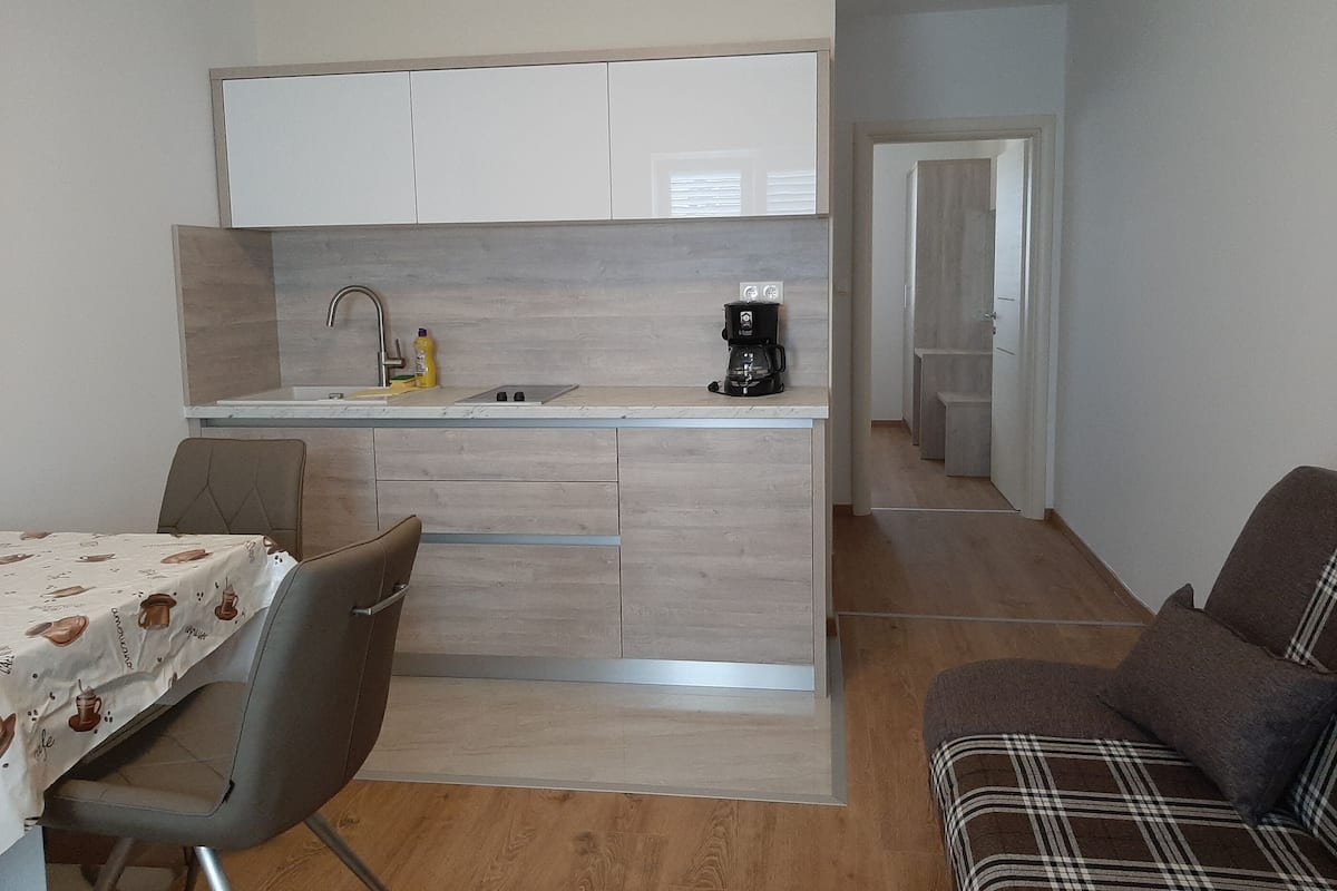 A compact kitchen with a sink, coffee maker, and a table with a coffee-themed tablecloth.
