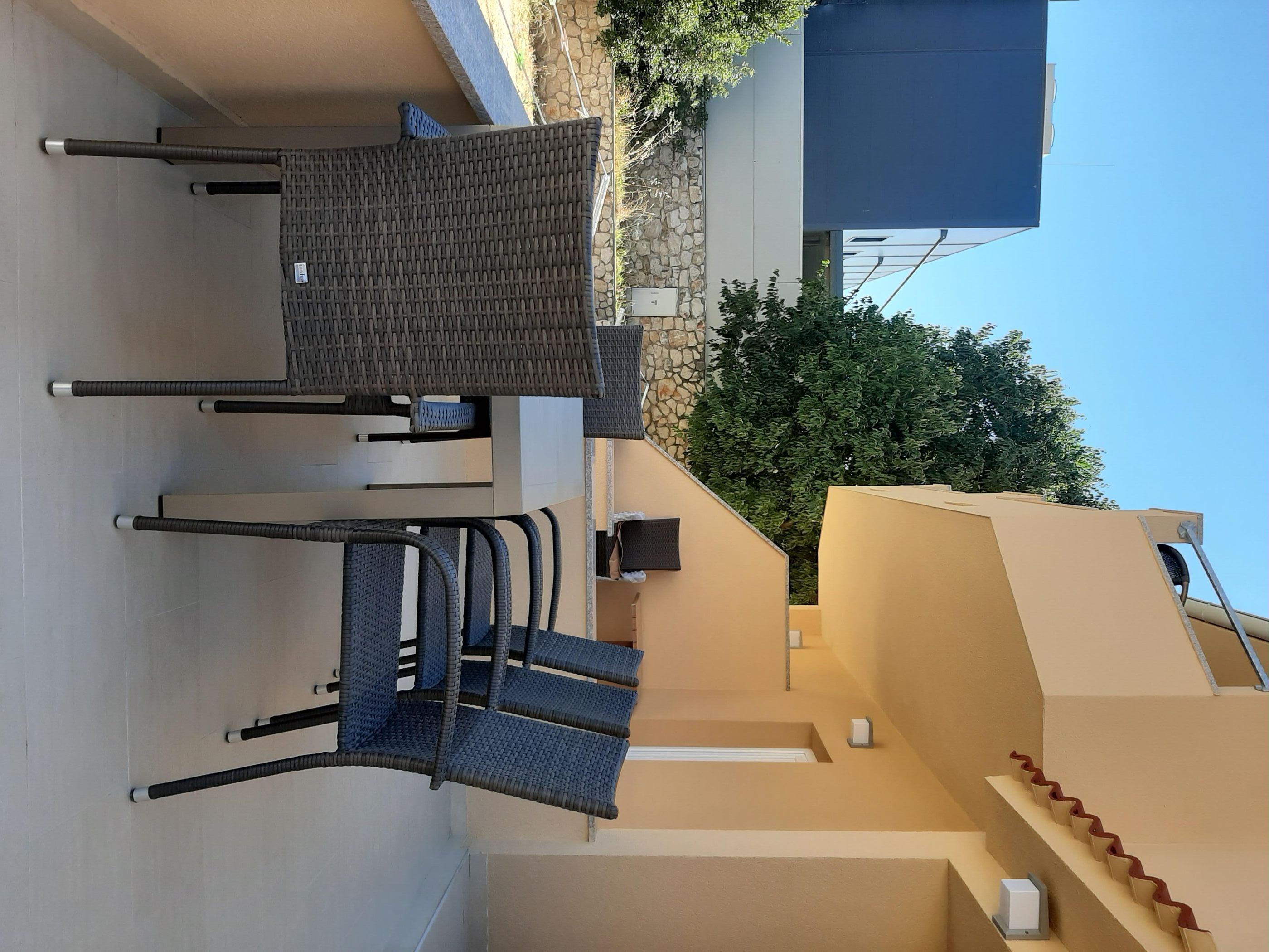 Eine Terrasse mit Gartenmöbeln, einer Steinmauer und einem Baum.