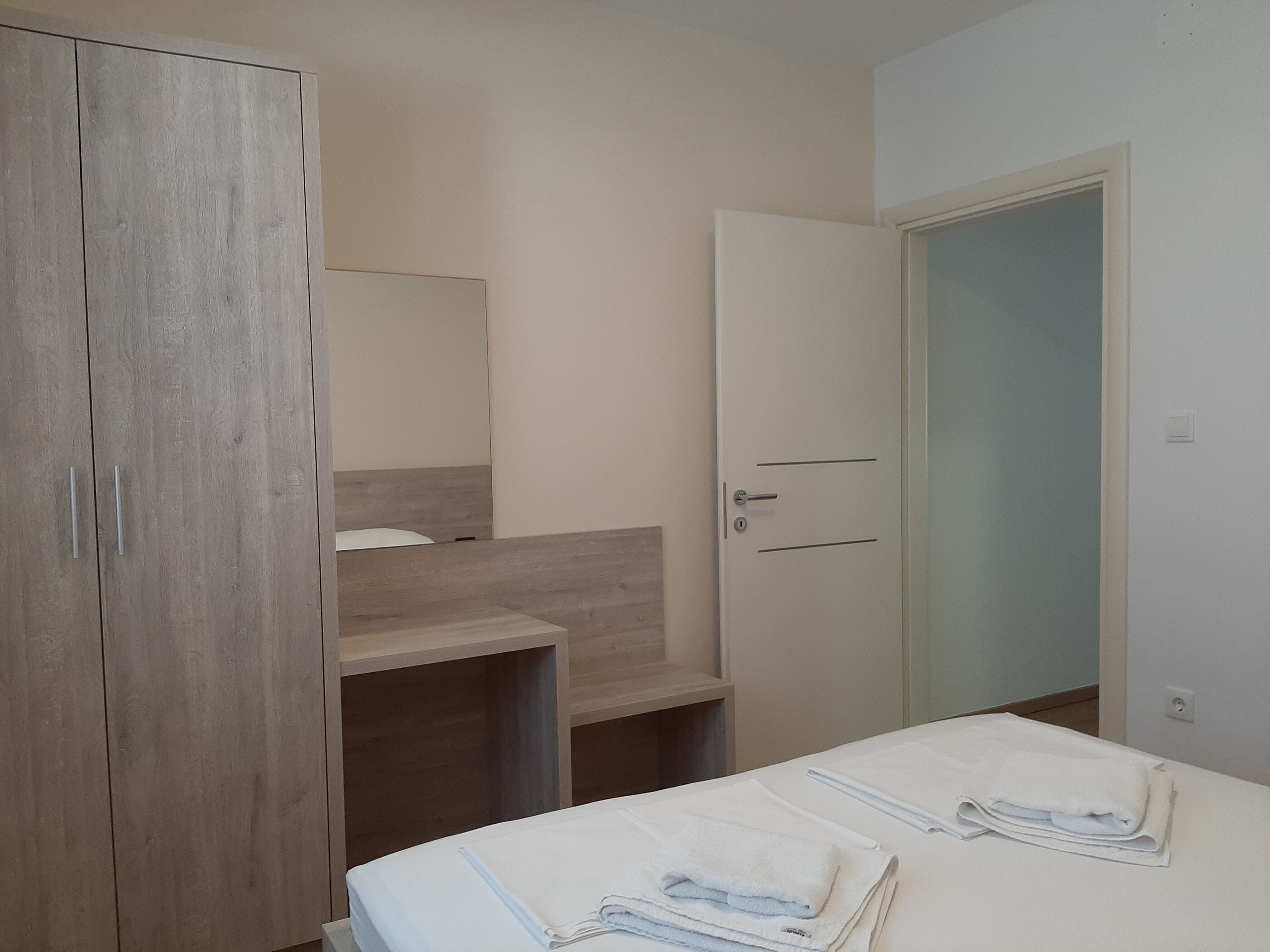 A modern bedroom with a wooden wardrobe, a bedside table, and a door.