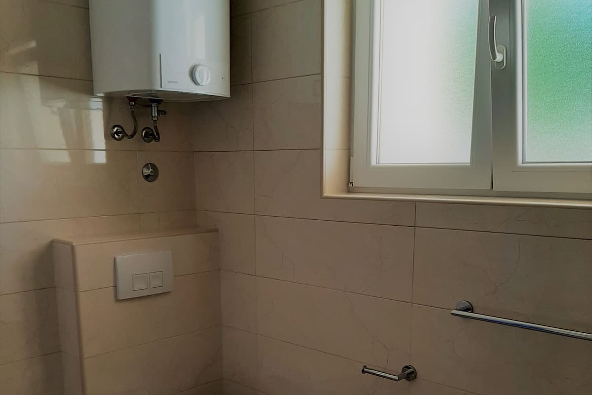 A small, compact bathroom with a toilet, a towel rack, and a window.