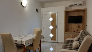 Un comedor con mesa y sillas, un sofá, un televisor y un equipo de aire acondicionado.