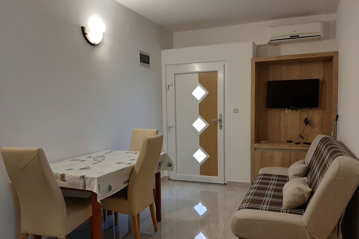 A dining area with a table and chairs, a sofa, a television, and an air conditioning unit.