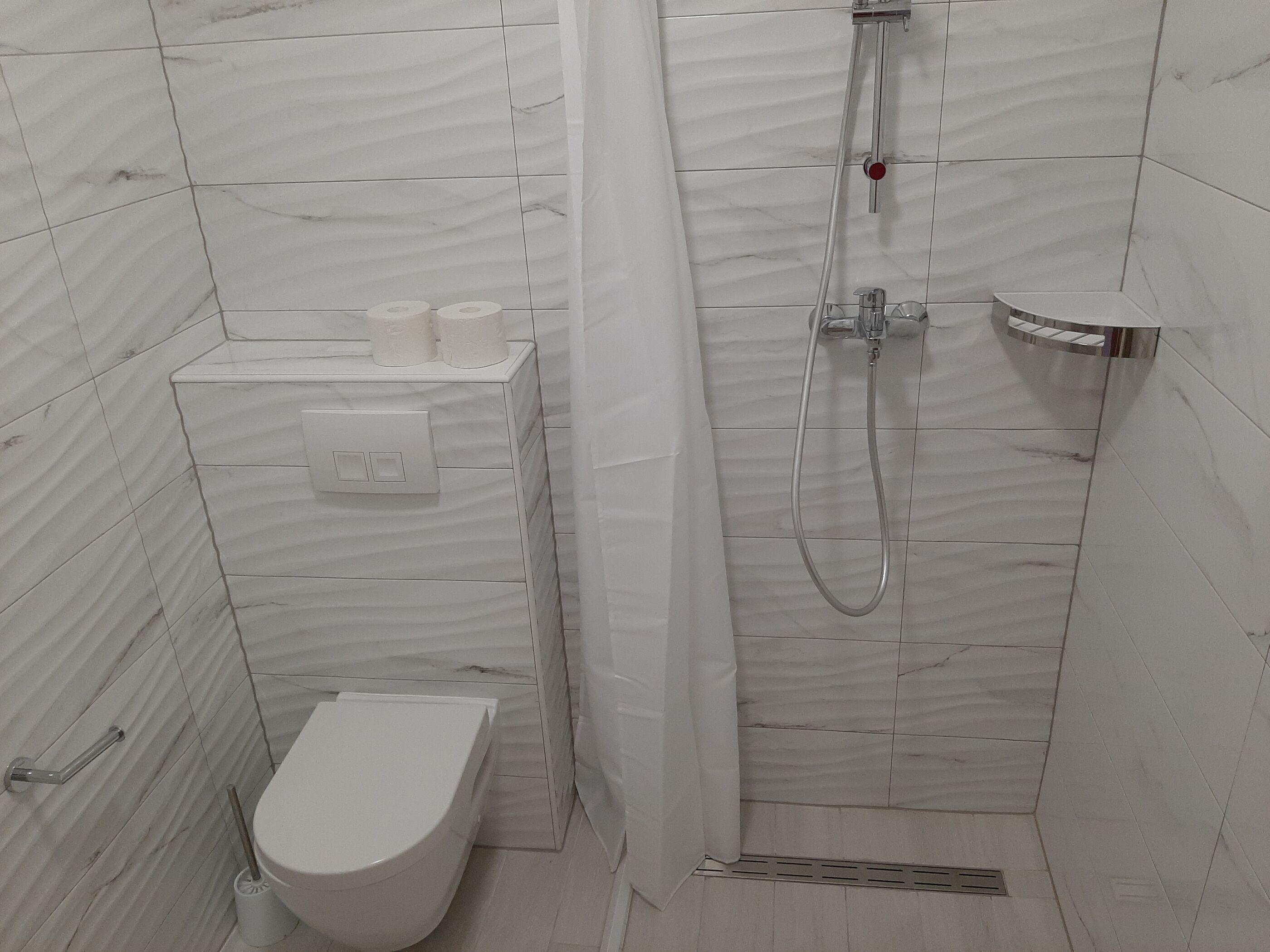 A small, modern bathroom with a toilet, a shower, and a sink.