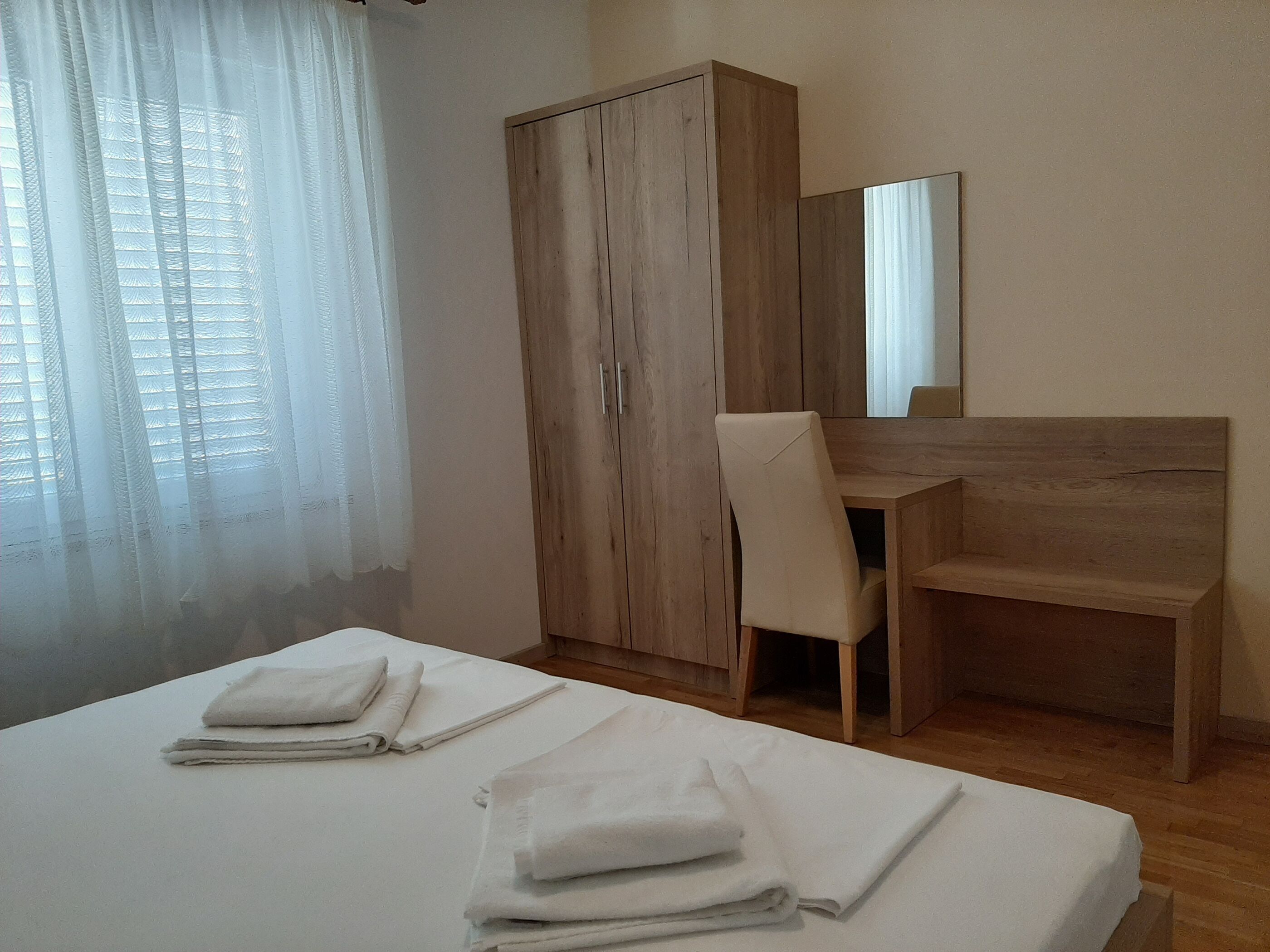 A bedroom with a bed, a wooden wardrobe, a desk, and a chair.