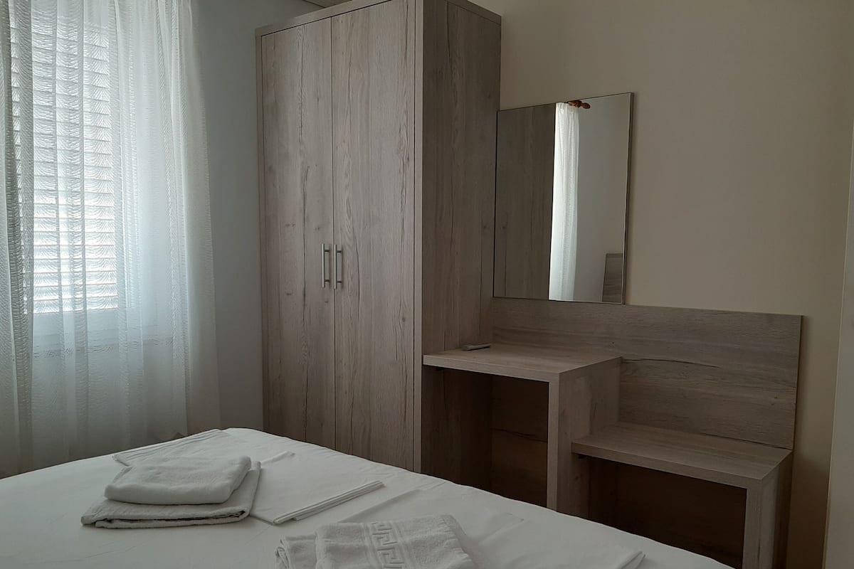 A bedroom with a bed, a wooden wardrobe, a bedside table, and a mirror.