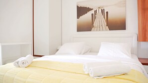Ett hotellrum med en säng, vita sängkläder, en gul filt och en tavla som föreställer en brygga på väggen.