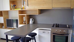 Ett modernt kök med träskåp, en inbyggd diskmaskin, en spis och en platt-TV.
