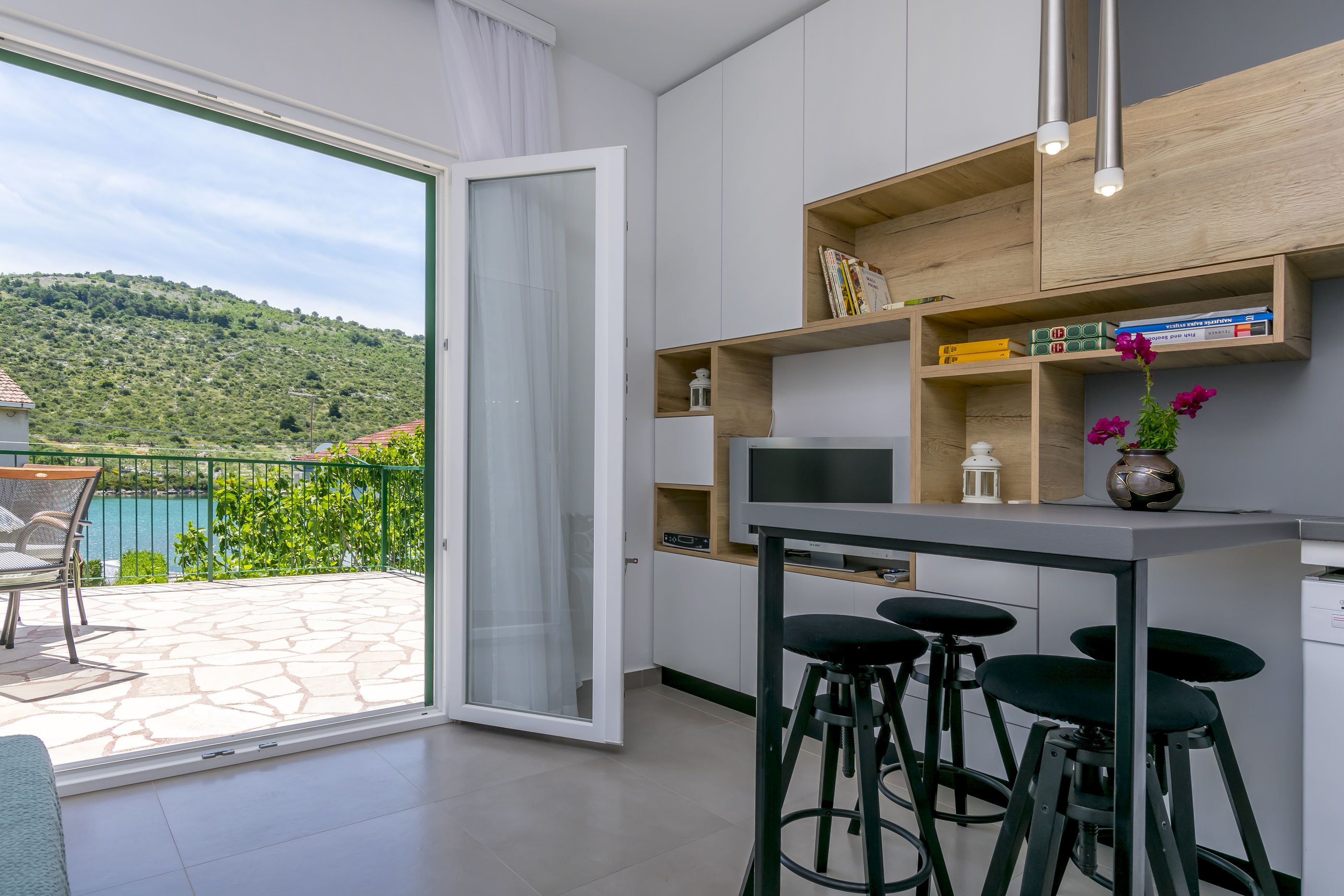 Eine moderne Küche mit einem großen Fenster, einer Bar mit Hockern und Blick auf eine gebirgige Landschaft.