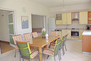 A dining area with a glass-top table, six chairs, and a vase with flowers.
