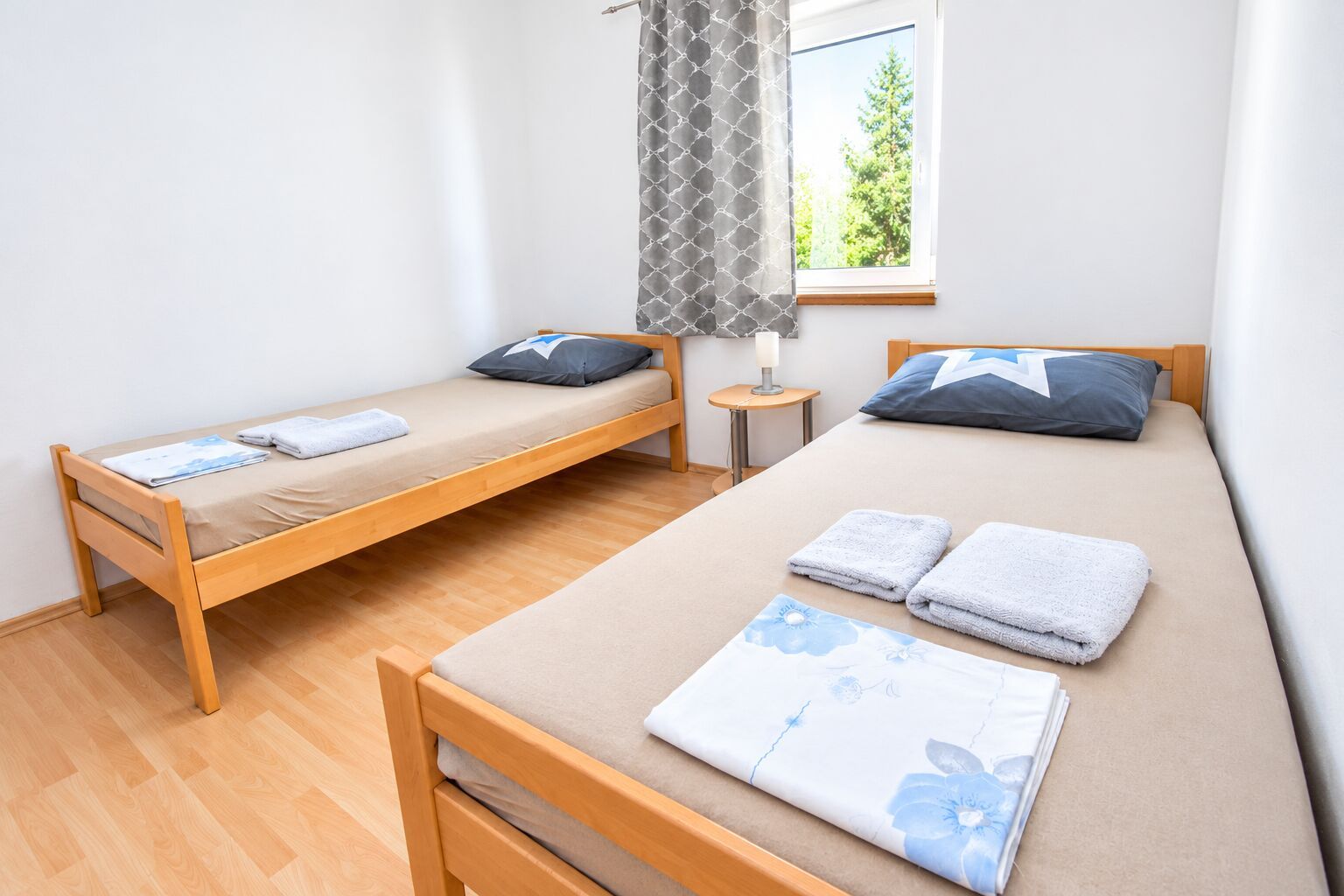 A room with two single beds, a small table, and a window with a view of trees.