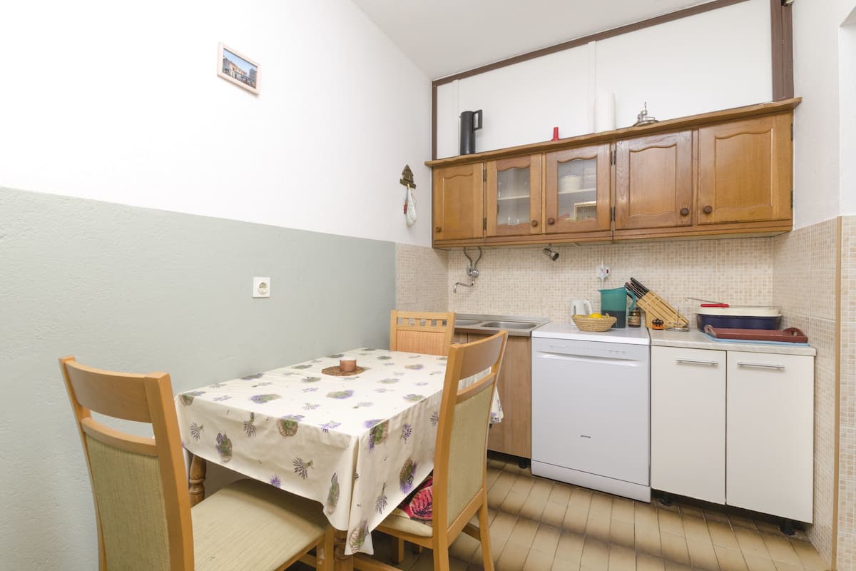 Una piccola cucina con mobili in legno, una lavastoviglie bianca e un tavolo con una tovaglia a fiori.