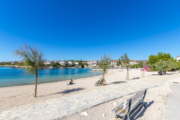 A coastal beach with a stone pathway, a bicycle, and a person sunbathing.